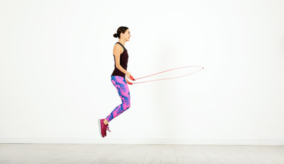 Wall Mural - Young sportive woman training with jump rope in light room