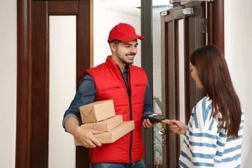 Young woman with credit card using bank terminal for delivery payment at doorway