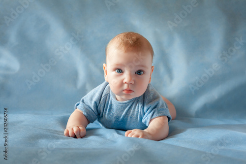 Fotografie, Obraz Beautiful baby lying on a blue background and smiling