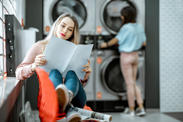 Wall Mural - Young woman waiting for the clothes to be washed sitting on the chair at the self-service laundry