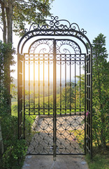 Sunset through the bars of wrought iron gate at hillside.