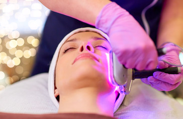 people, beauty, cosmetic treatment, cosmetology and technology concept - beautician with microdermabrasion device doing face exfoliation to young woman lying at spa