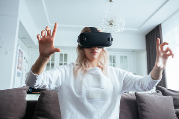 Young blonde at home with a modern design puts on virtual reality glasses