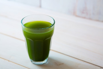 glass of green vegetable beverage on white wooden background