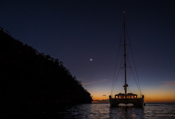 Wall Mural - Dark night view on sailing boat anchored on open sea with black silhouette of island