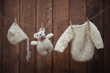 Baby Clothes And Teddy Hanging On Wooden Background