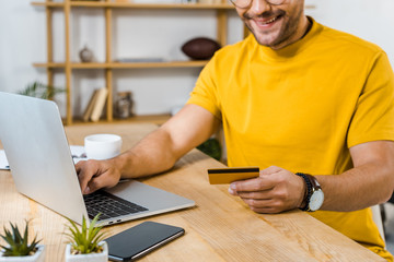 cropped view of man holding credit card near laptop