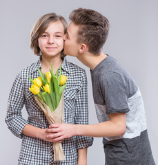 Boy Giving Flowers for Girl. Holidays, Love, Happiness and People concept - Happy Child celebrating Valentines Day. Teen Boy kisses a Girl.