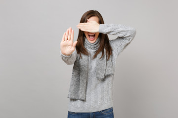 Screaming woman in sweater scarf covering eyes with hand showing stop gesture with palm isolated on grey background. Healthy fashion lifestyle people emotions, cold season concept. Mock up copy space.