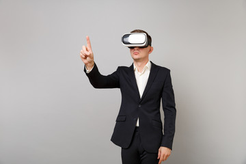 Young business man in suit looking in headset touch something like push click on button and pointing at floating virtual screen isolated on grey background. Achievement career wealth business concept.