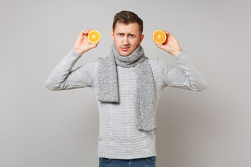 Wall Mural - Discouraged young man in gray sweater, scarf holding oranges isolated on grey background, studio portrait. Healthy fashion lifestyle, people sincere emotions, cold season concept. Mock up copy space.