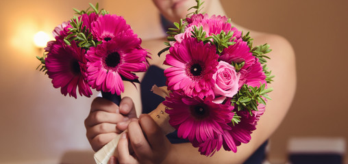 A beautiful bridesmaid holding a bouquet of warm pink beautiful organic natural flowers into the camera with a shallow depth of field. conceptual image for a wedding celebration.