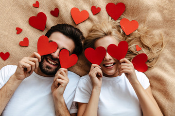 couple. love. valentine's day. man and woman are holding red paper hearts and smiling; top view