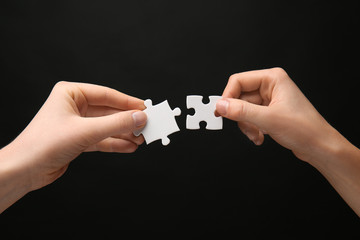 Female hands with pieces of puzzle on dark background