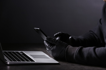 Professional hacker with laptop and mobile phone sitting at table on dark background