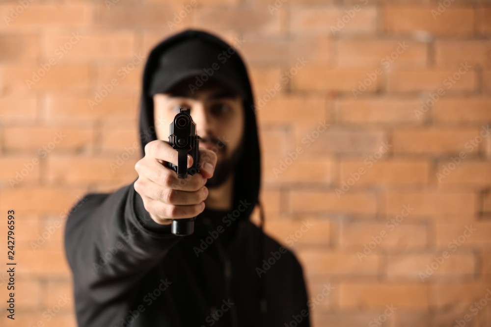 Male criminal pointing a gun at viewer against brick background