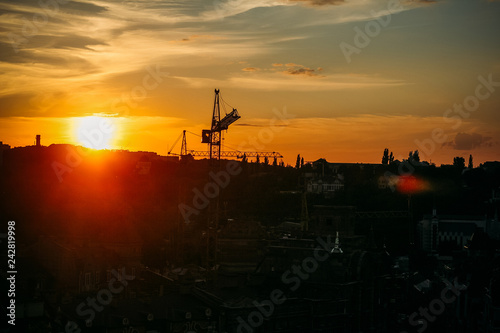 Fotografie, Obraz Urban industrial construction of steel tower cranes on sunset with sky