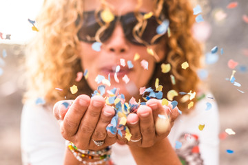 Close up of woman's habd and beautiful lady blowing out coloured carnival party confetti - focus on colors papers and hapiness and joyful lifestyle concept for happy people outdoor