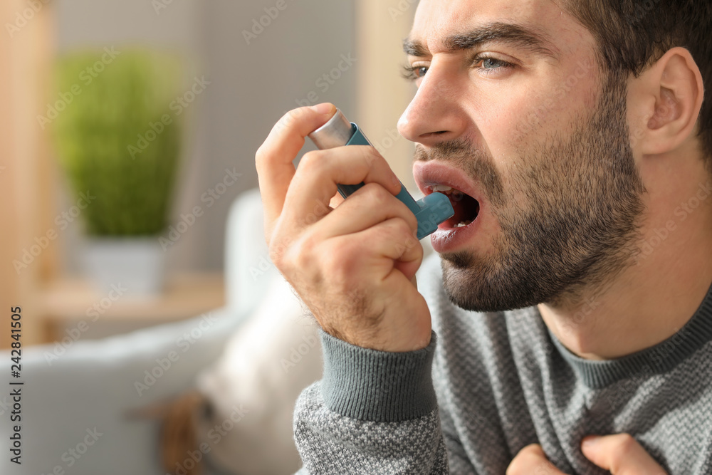 Young man with inhaler having asthma attack at home