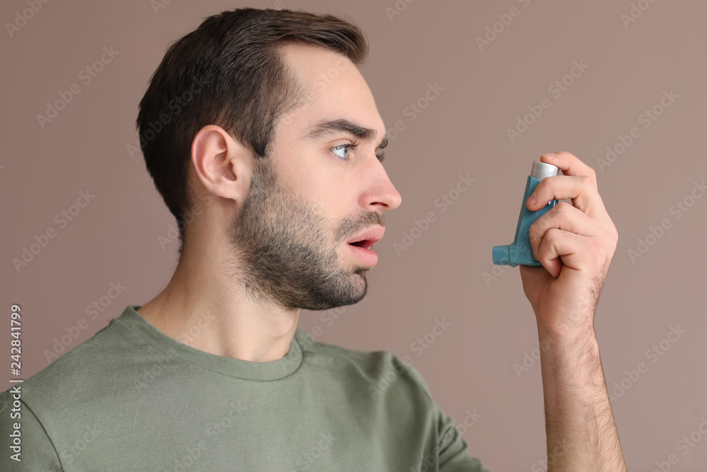 Young man with inhaler on color background