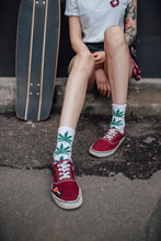 Woman's Legs In Socks And Sneakers Sitting Next To Carver Skateboard