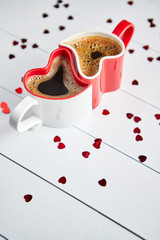 Two, red and white, heart shaped, connected coffee cups placed on wooden background with sequins. Valentines or love concept. Flat lay, top view.