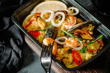 Seafood Paella in black box. Healthy food and diet concept, restaurant dish delivery. Take away of fitness meal. Weight loss nutrition in boxes.