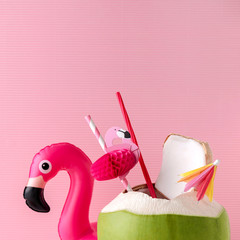 Wall Mural - Fresh coconut on a pastel pink background with flamingo inflatable drink holder, summer vibes concept