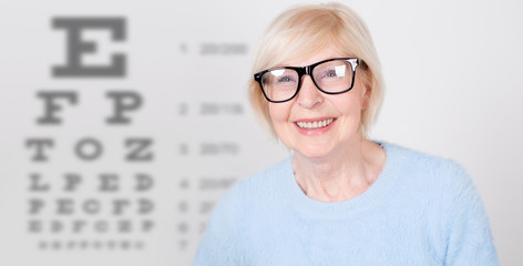 Senior woman in glasses having eye on the vision testing tables background. Visiting a doctor ophthalmologist.