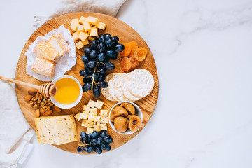 Wall Mural - Flat lay with various types of cheese, grapes, nuts, honey and cracker in wooden board on marble