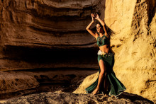 Young Girl In Green Dress Dancing The Famous Belly Dance, In The Mythical Space Of The Canyons Of The Namibe Desert. Africa. Angola.