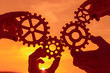 © gerasimov174 - gears in the hands of people on the background of the evening sky. the mechanism of teamwork.
