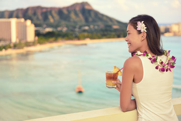 Hawaii vacation summer travel- Mai Tai and aloha spirit. Asian woman relaxing drinking Hawaiian cocktail drink Mai Tai, at sunset view of Waikiki beach in Honolulu, Oahu, USA travel.