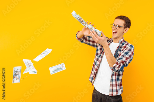 Fotomural happy man, wearing glasses and a plaid shirt, throwing out money banknotes on a