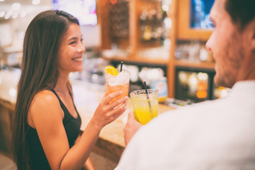 Bar drinking cocktails dating couple lovers talking with drinks at restaurant at night. People at restaurant with alcoholic cocktail beverage. Asian woman smiling.