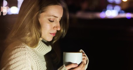 Wall Mural - Beautiful young woman in cozy warm sweater with cup of hot drink on blurred background
