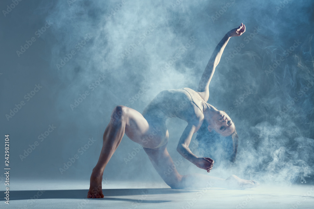 Dancing in cloud concept. Muscle brunette beauty female girl adult woman dancer athlete in fog smoke fume wearing dance bodysuit making emotional dance element performance on isolated grey background - obrazy, fototapety, plakaty 
