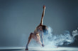 Dancing in cloud concept. Muscle brunette beauty female girl adult woman dancer athlete gymnast in smoke / fog wearing dance bodysuit making dance element performance on isolated grey black background