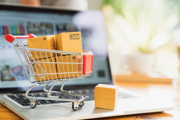 Online shopping and delivery concept, product package boxes in cart and laptop computer on table with copy space.