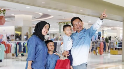 Wall Mural - Happy family standing in the shopping mall while holding shopping bags and looking at a store. Shot in 4k resolution