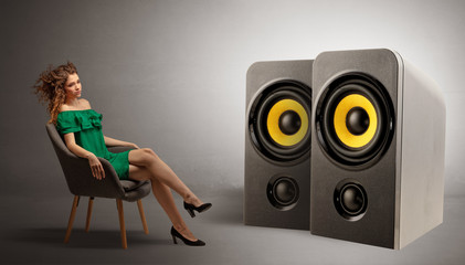 Stylish young lady sitting in a sofa and listening to big loudspeakers
