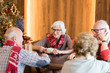 © Seventyfour - Group of positive elderly friends in scarves with Christmas patterns sitting at table and chatting while drinking coffee at Christmas eve