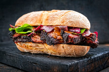Traditional Barbecue Pulled Pork Piece Of Bosten Butt As Sandwich With Lettuce As Closeup On A Black Board
