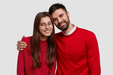 Portrait Of Young Family European Couple Wear Red Clothes, Pose For Making Common Photo, Have Good Relationships, Warm Cuddle, Isolated Over White Studio Background. People And Relations Concept