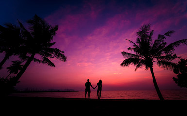 Silhouette of couple on tropical beach during sunset on background of palms and sea