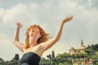 Freudig glückliches Portrait einer jungen eleganten rothaarigen lockigen Frau mit erhobenen Armen am Meer am Strand in Ligurien Italien mit Textfreiraum, Platz für Text 