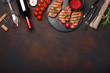 Grilled pork steaks on stone with bottle of wine, wine glass, knife and fork on rusty background. Top view with space for your text.