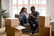Happy african american couple feeling excited on moving day, black family tenants laughing celebrating relocation sitting on sofa with boxes, home owners having fun in new house together concept