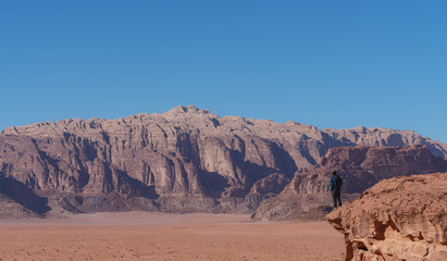 Wall Mural - traveler standing on edge of mountain cliff, at wadi rum desert in jordan. travel lifestyle and adve
