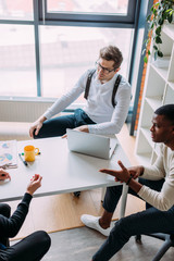 Canvas Print - Multiracial group of young people in formal wear making out business plan for future start-up project sitting at the desk. Corporate Work Concept . Top view.